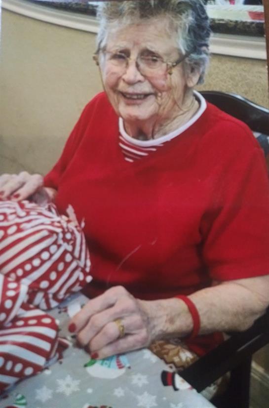 Elderly woman focuses on sewing a vibrant fabric in a well-lit room while smiling.