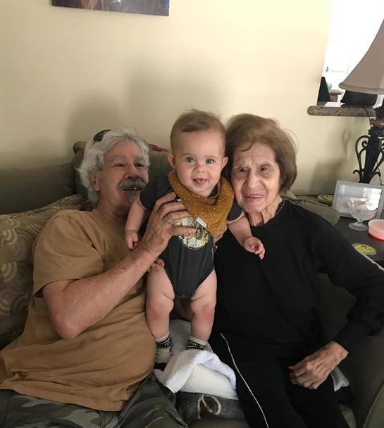 Two elderly people happily embrace their cheerful baby grandson, showcasing a moment of family love.
