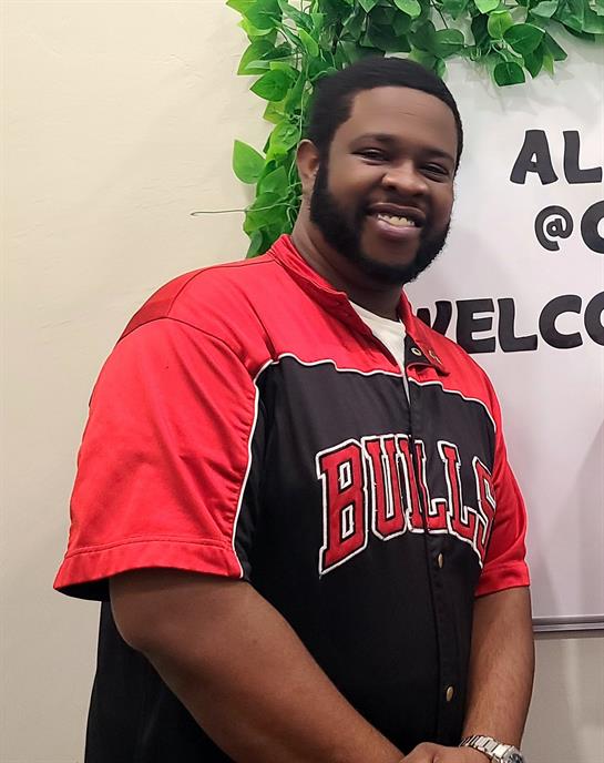 A joyful individual dressed in red and black stands confidently at a community event.