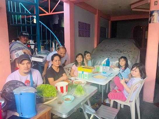 A group of people is seated at tables sharing food and conversations in a vibrant outdoor setting.