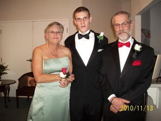 Three people dressed in formal attire pose together at a celebration with corsages and smiles.