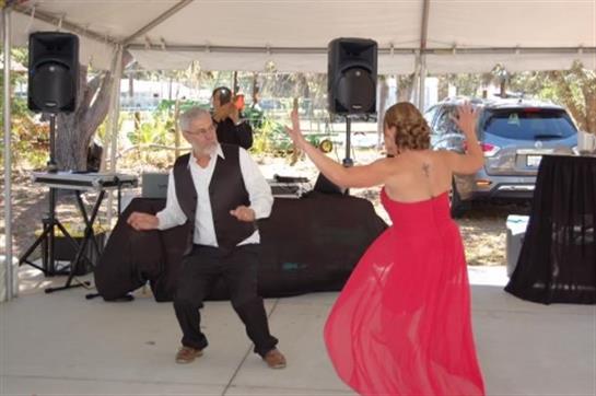 A couple enjoys dancing under a tent during a festive gathering with music playing nearby.