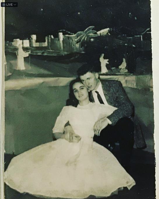 A couple enjoys a romantic moment sitting together, dressed formally in vintage clothing at night.