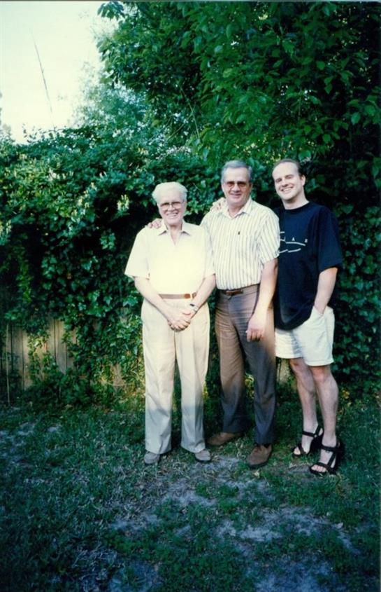 Three people smile and enjoy each other's company in a colorful garden.