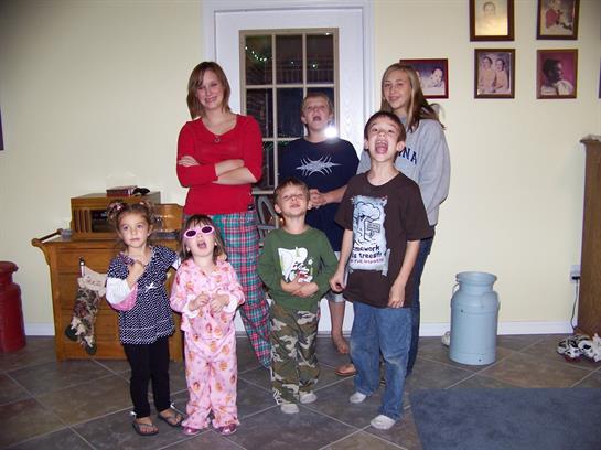 A group of kids and adults smile together in a cozy, inviting living room.