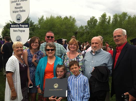 Group of family members smiling together after a graduation ceremony in a park setting.