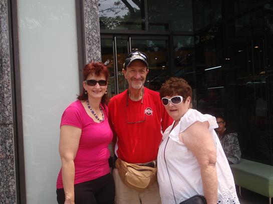 Three friends smile and pose at a cafe entrance on a bright day.