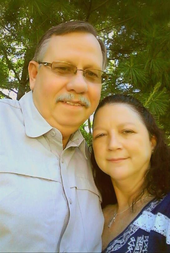 A couple takes a joyful selfie in a vibrant garden, surrounded by greenery during daylight.