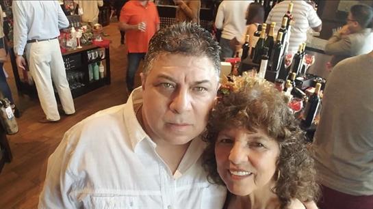 Couple smiles together at a bustling venue filled with wine bottles and lively guests.