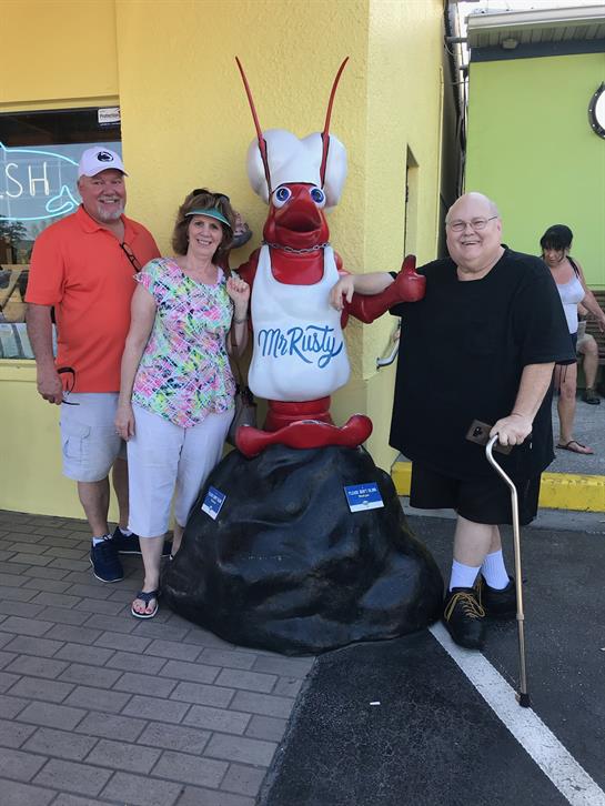 Friends take a fun photo with a colorful lobster statue outside a restaurant on a sunny day.