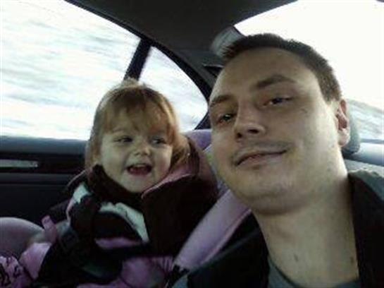 A father and his young daughter smile at each other inside a car during winter.