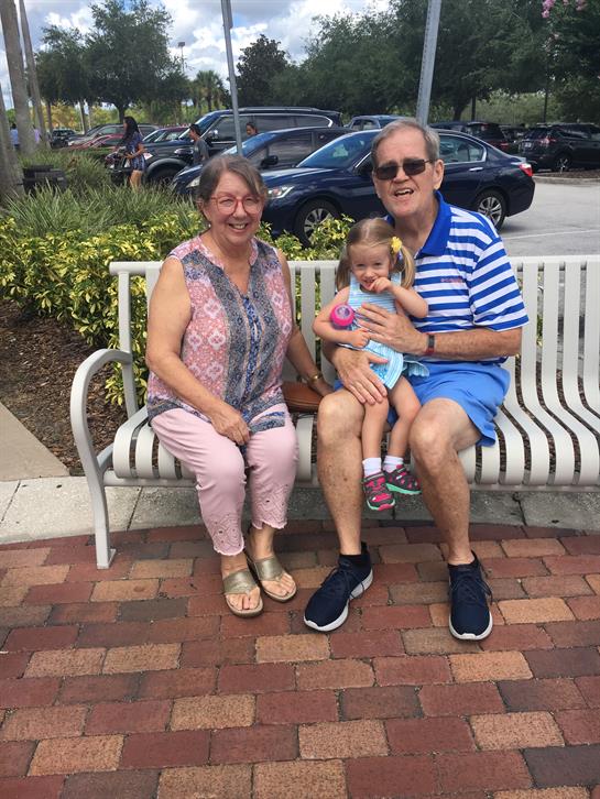 An elderly couple sits together with their granddaughter at a park, smiling and relaxed.