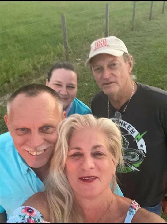 Four friends smile together while enjoying a casual outdoor gathering in a grassy area.
