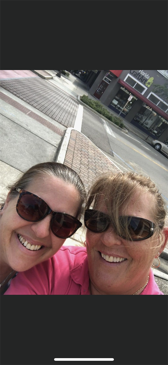 Two friends take a cheerful selfie on a sunny day, capturing their joyful moment on the street.