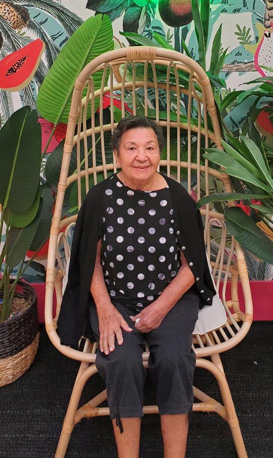 A woman smiles as she sits comfortably in a unique hanging chair surrounded by vibrant greenery.