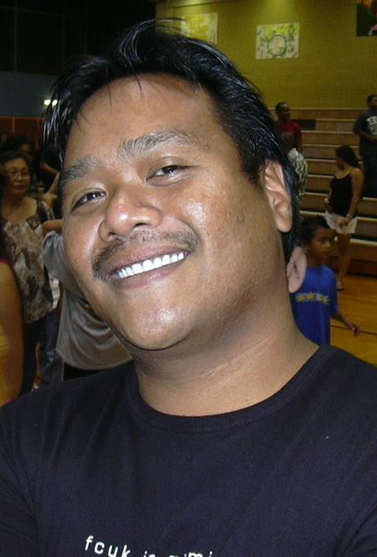 A joyful man with a friendly smile stands in a crowded gymnasium at a community gathering.