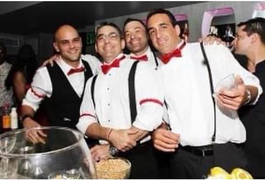 Four men in formal attire with bow ties smile and pose together at a celebratory gathering.