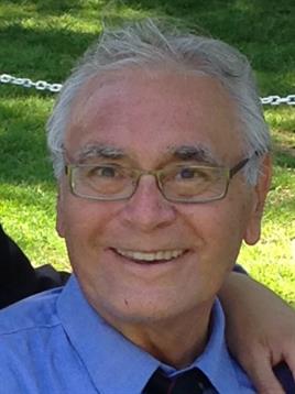 Elderly man with glasses smiles happily while spending time outdoors with friends.