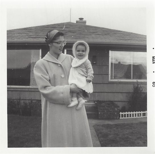 A mother smiles proudly while holding her infant daughter in a suburban setting.