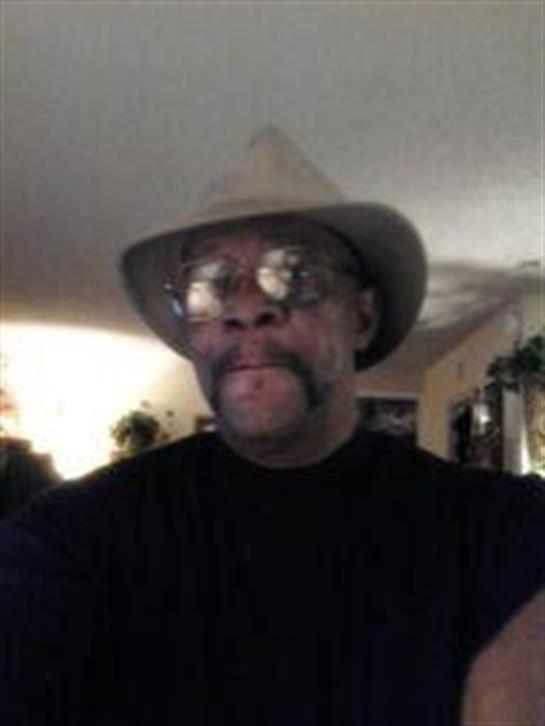 A middle-aged man with a mustache is smiling while wearing glasses and a hat indoors.