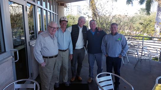 Five friends pose together on a patio, enjoying each other's company in bright weather.