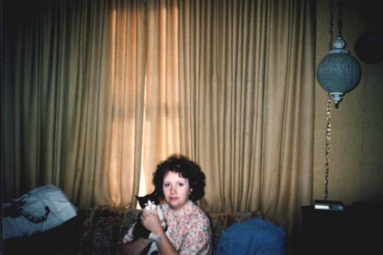 A child with curly hair sits on a couch, gently holding a cat in a warm and inviting living space.