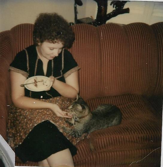 A woman dining on the couch while playfully interacting with a cat nearby in a warm room.