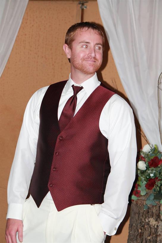 A stylish man in a dark vest and white shirt poses at a beautifully decorated venue.
