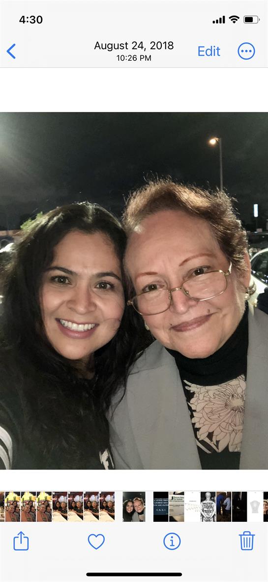 Two women smile happily together at night, showcasing their bond in a lively parking area.