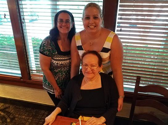 Three women smile together at a table in a restaurant, enjoying each other's company.
