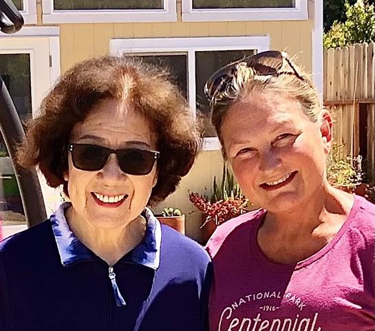 Two women stand together in a bright garden, highlighting friendship and joy in the sunshine.