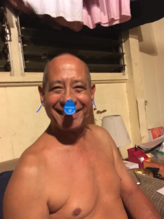 A cheerful man enjoys his time indoors, playfully posing with a blue cap on his nose.