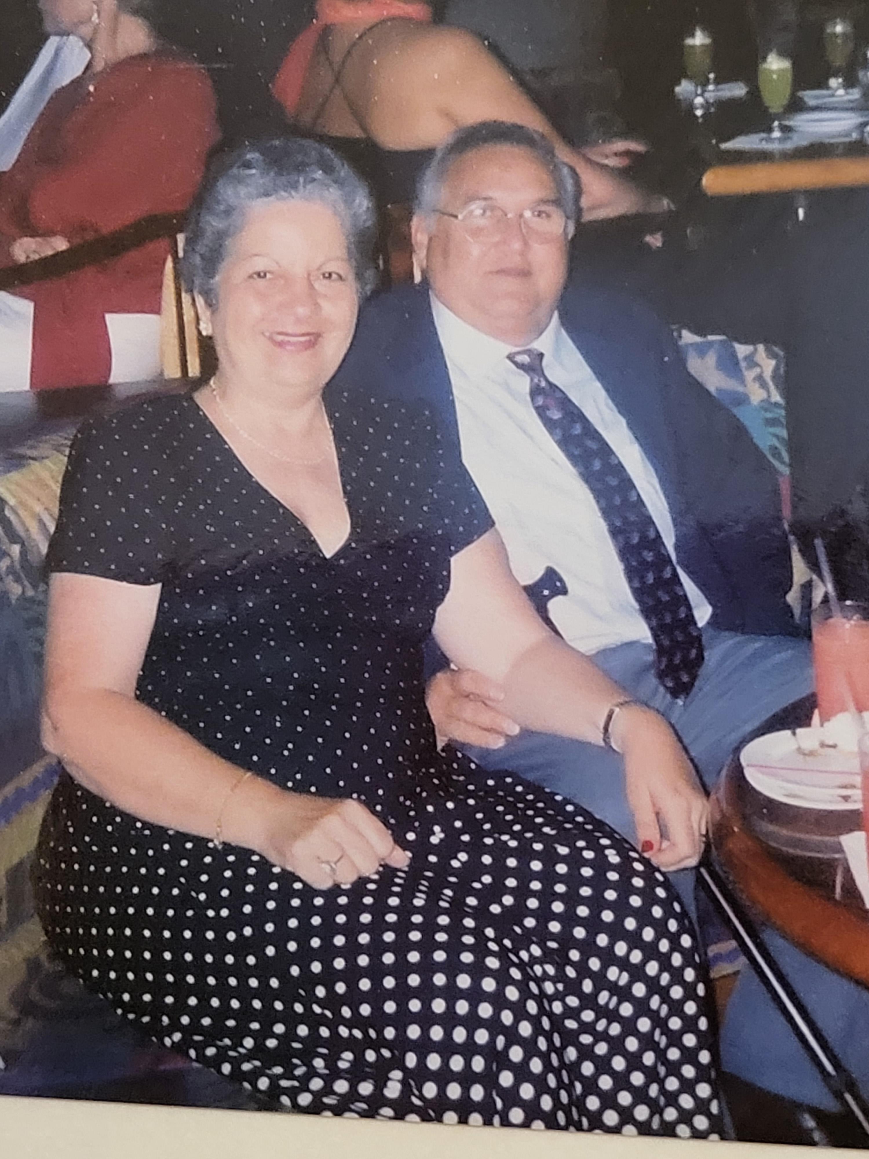 A cheerful couple sits close together, smiling and enjoying their time at a lively social event.