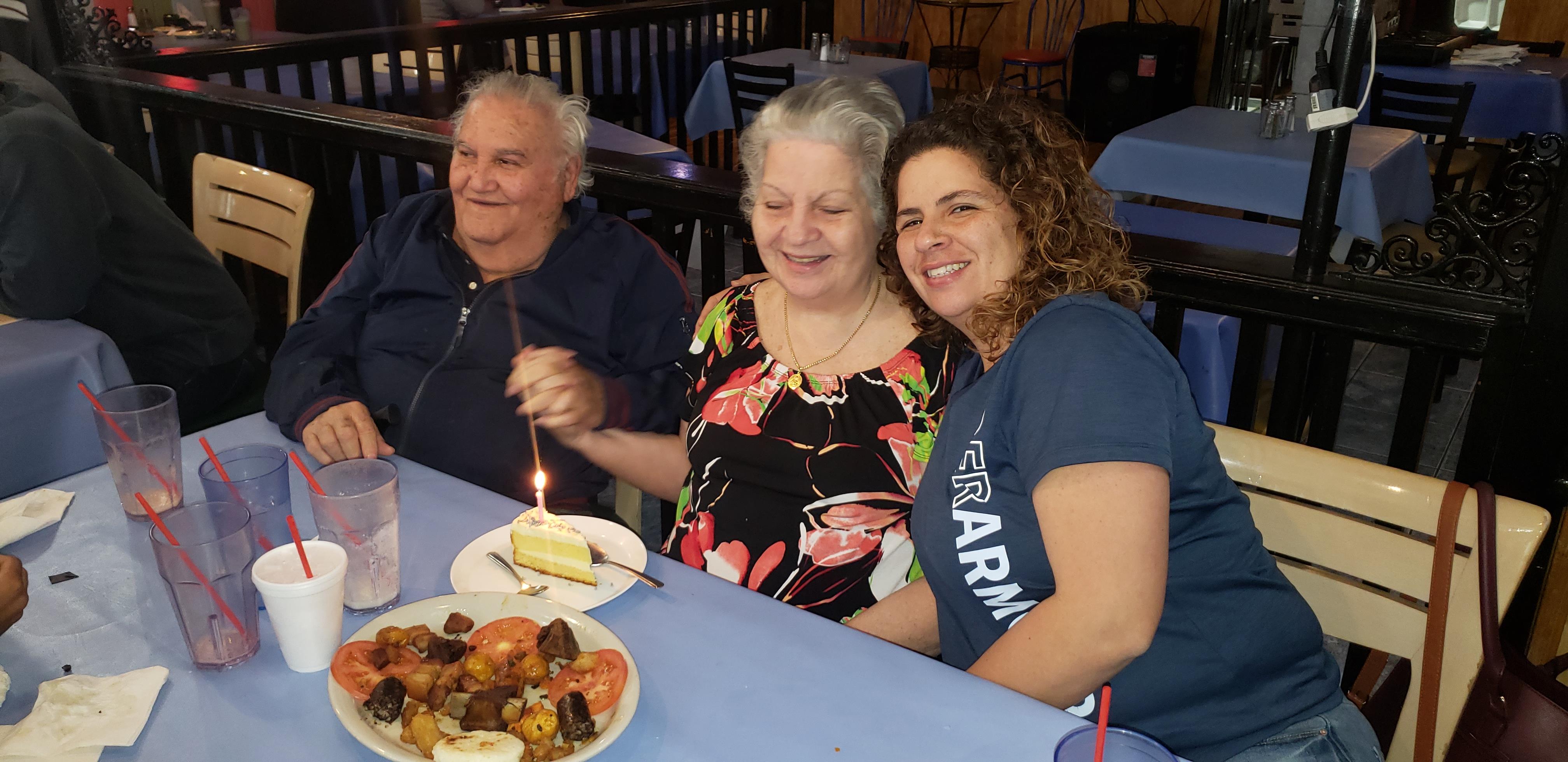 Friends and family joyfully gather around a table, celebrating with food and dessert.