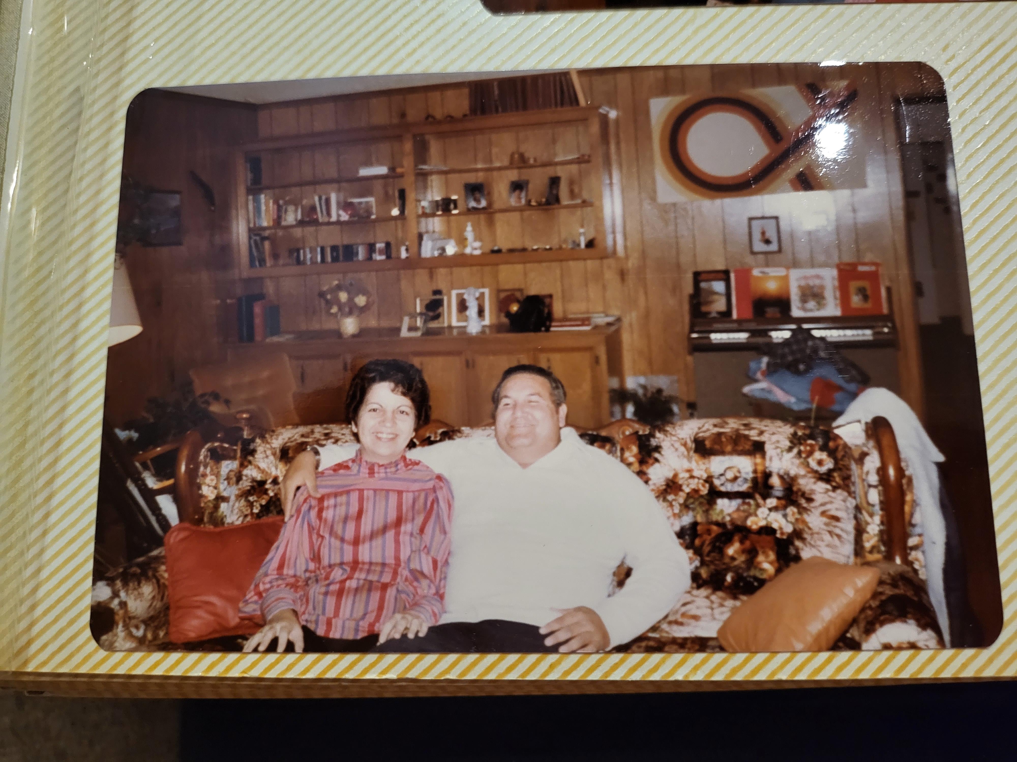 Two individuals pose happily on a floral couch in a vintage-inspired living room setting.