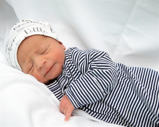 A peaceful newborn rests on white fabric, wearing a striped outfit and a charming hat.