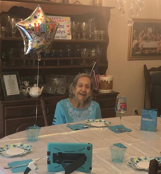 An elderly woman smiles at a festive table, enjoying the celebration.