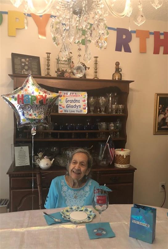 Elder woman smiles joyfully at her birthday celebration with a festive atmosphere and decorations.