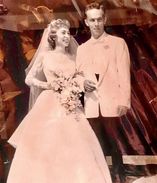 A happy couple stands together at their wedding, dressed in formal attire and smiling joyfully.
