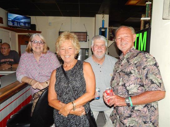 Four friends gather cheerfully in a garage, sharing laughs and drinks on a pleasant evening.