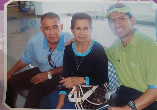 Two elderly people and a young man smile cheerfully in a lively airport waiting area.