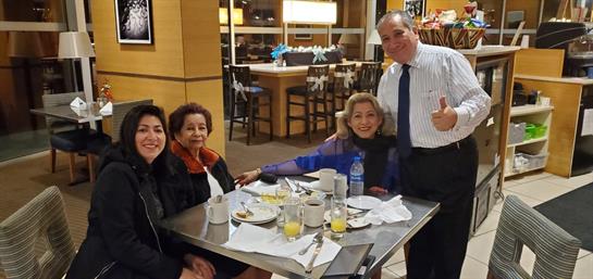 Four friends share laughter and stories over a breakfast spread in a lively restaurant.