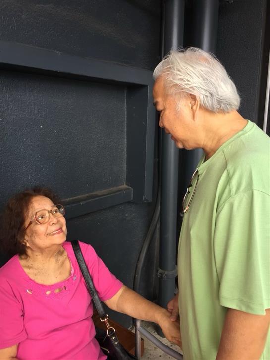Two friends smile and chat happily in the sun by the community center.