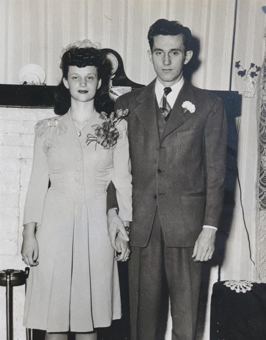Newlyweds stand together in formal wear, smiling at their wedding celebration in a classic setting.