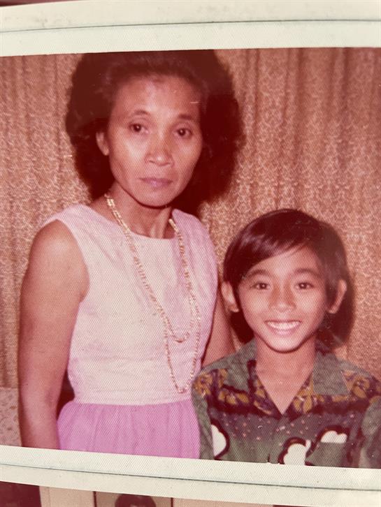 A woman and a boy smile warmly together in front of a textured backdrop.