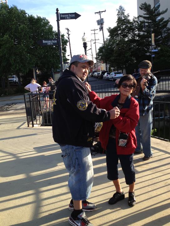 A couple poses playfully for a picture while others enjoy the evening in the background.