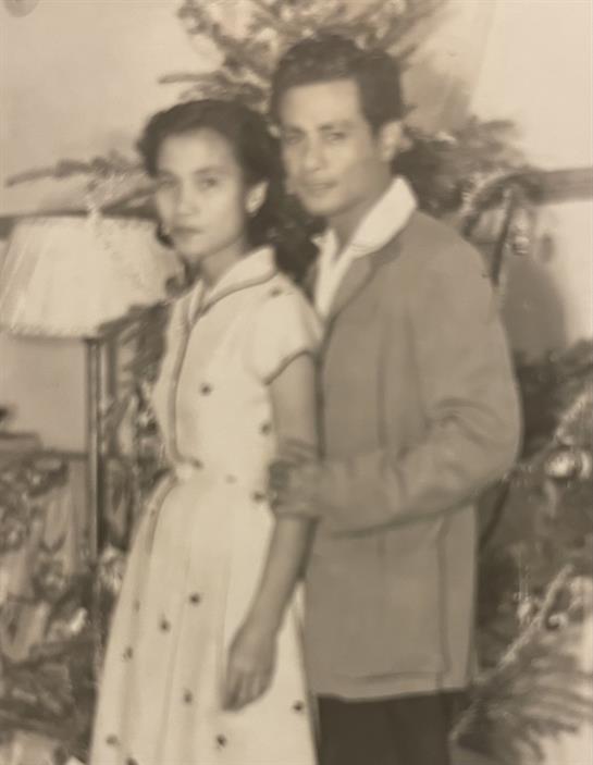 A man and woman pose closely in elegant vintage clothing, surrounded by festive decorations.