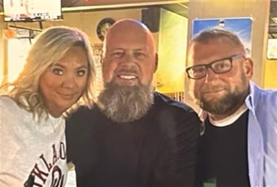 Three friends with joyful expressions pose together at a vibrant gathering in the evening.