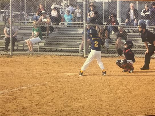 A young athlete stands ready to bat in a youth baseball game as spectators watch from the bleachers.