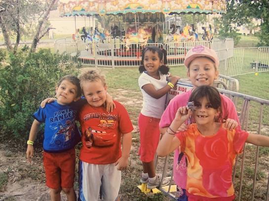 Group of children smiling and posing at a carnival filled with excitement and rides nearby.